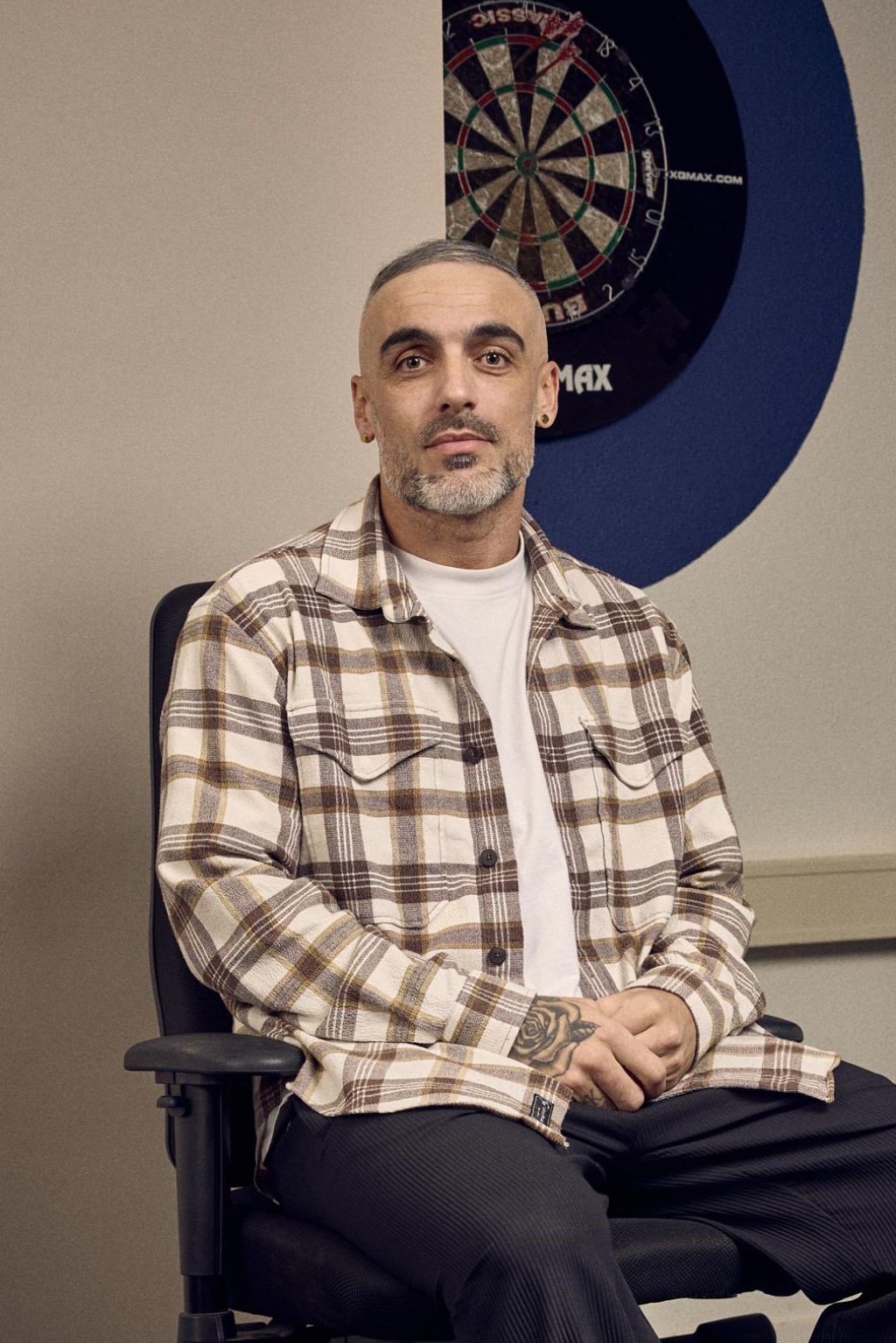 Antonio Stankov in een kantoorruimte zittend in een bureaustoel voor een bronzen backdrop en dartbord.