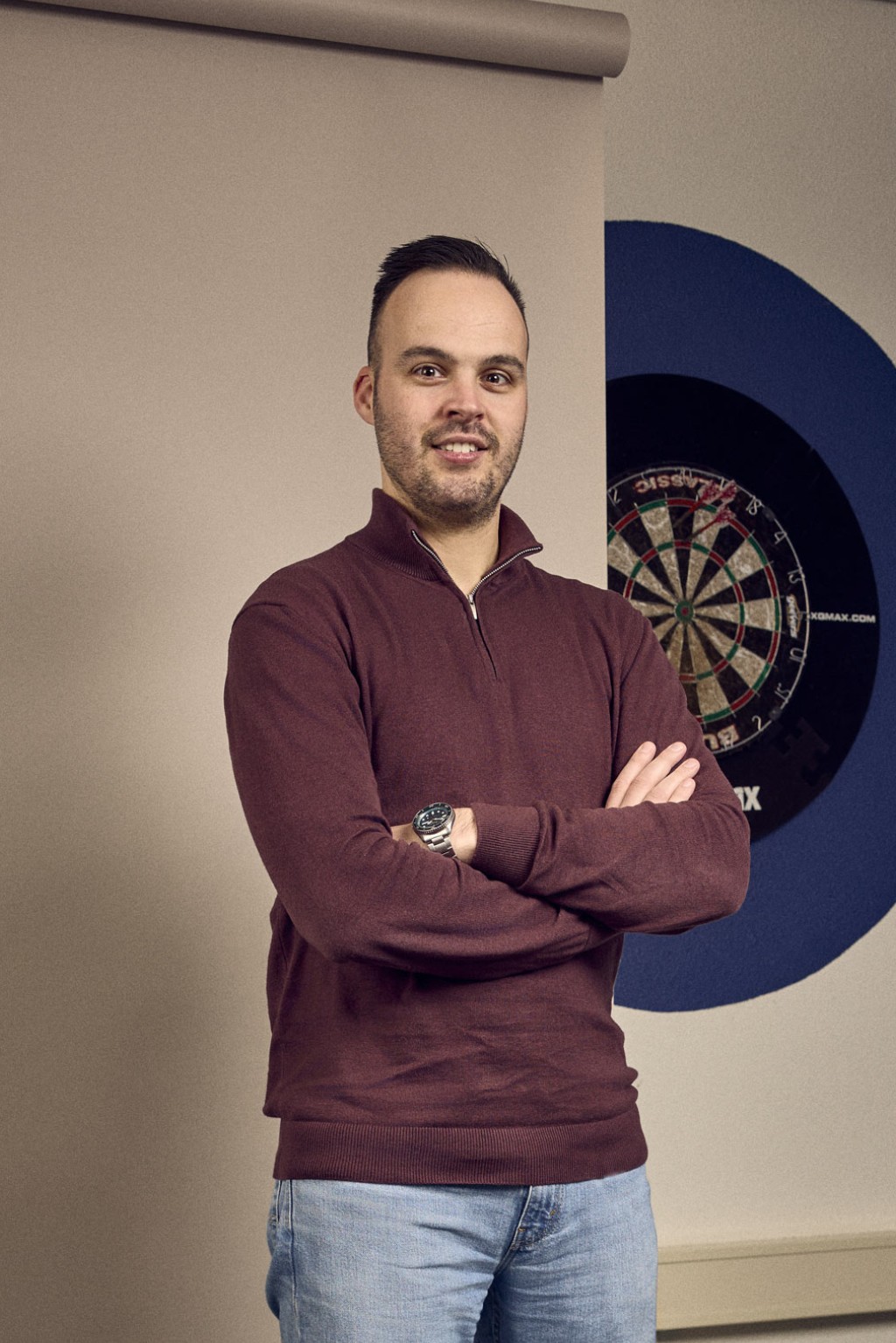 Bas Hendriks staat voor een bronzen backdrop en een dartbord.