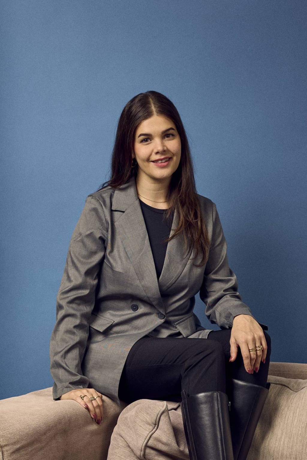 Carmen Klein voor een blauwe backdrop in een kantoorruimte, schuin zittend op de bank.