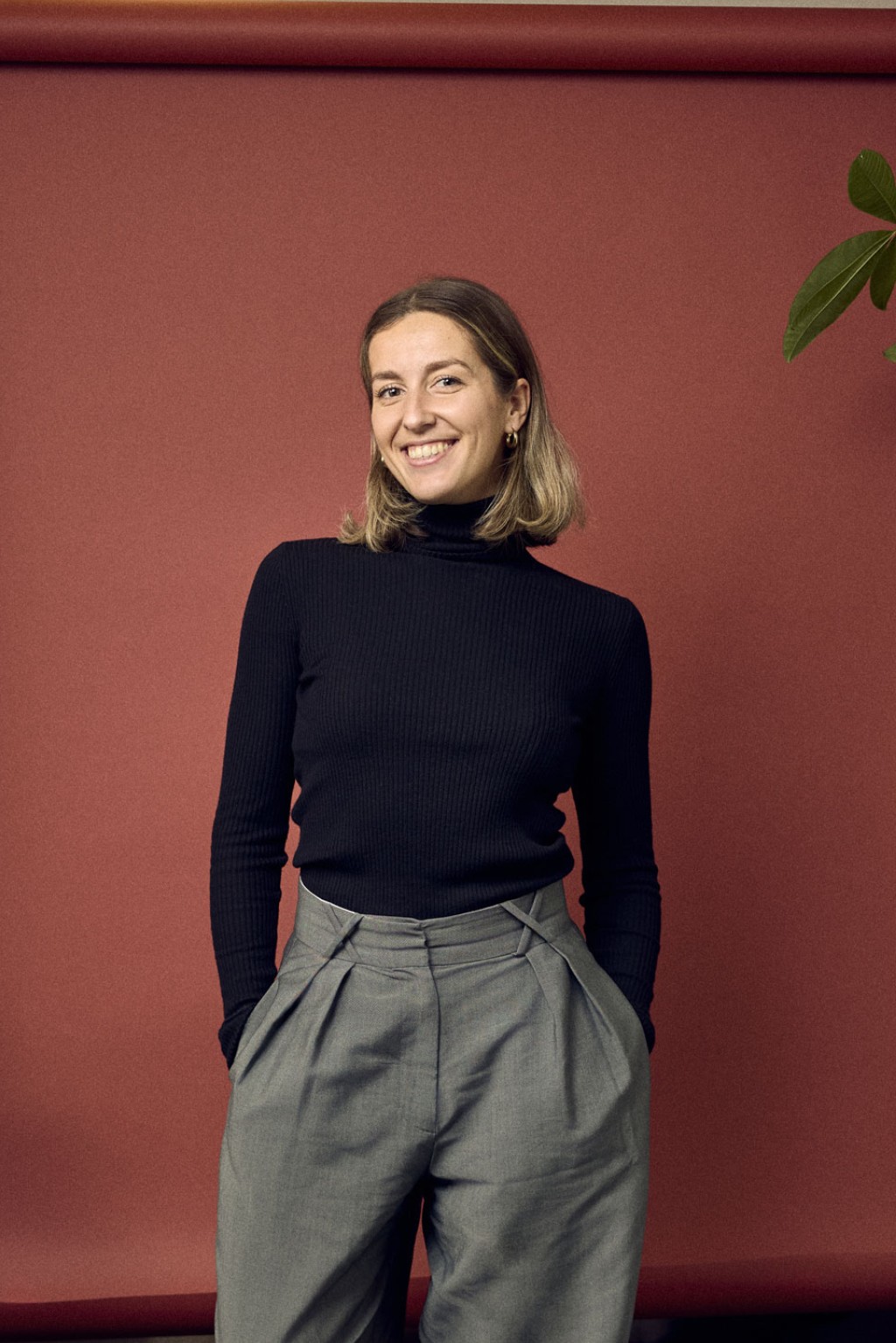 Eva Schoren staat voor een rode foto backdrop met een plant.