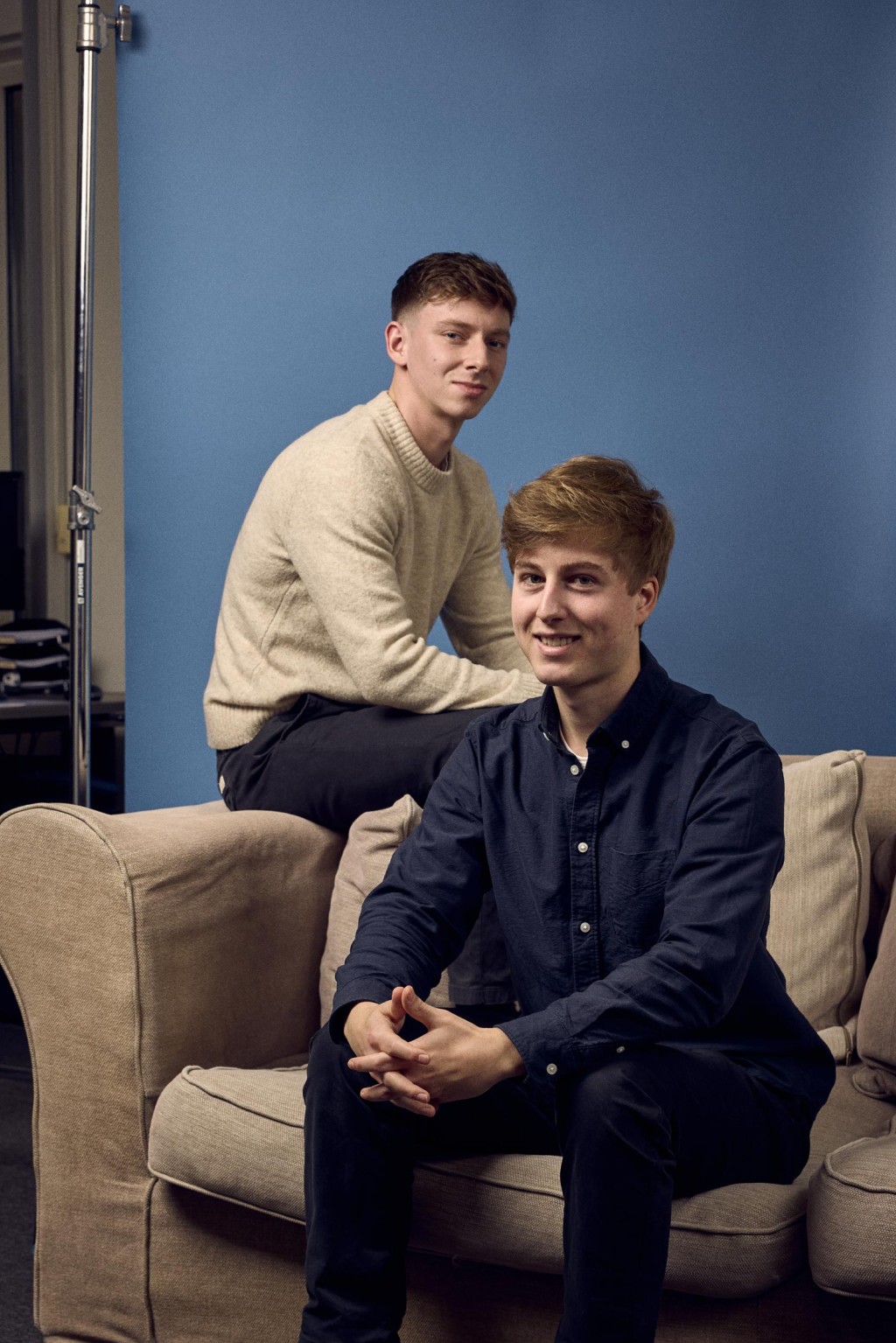 Lucas en Lodewijk zitten op een bank en poseren voor een blauwe foto backdrop.