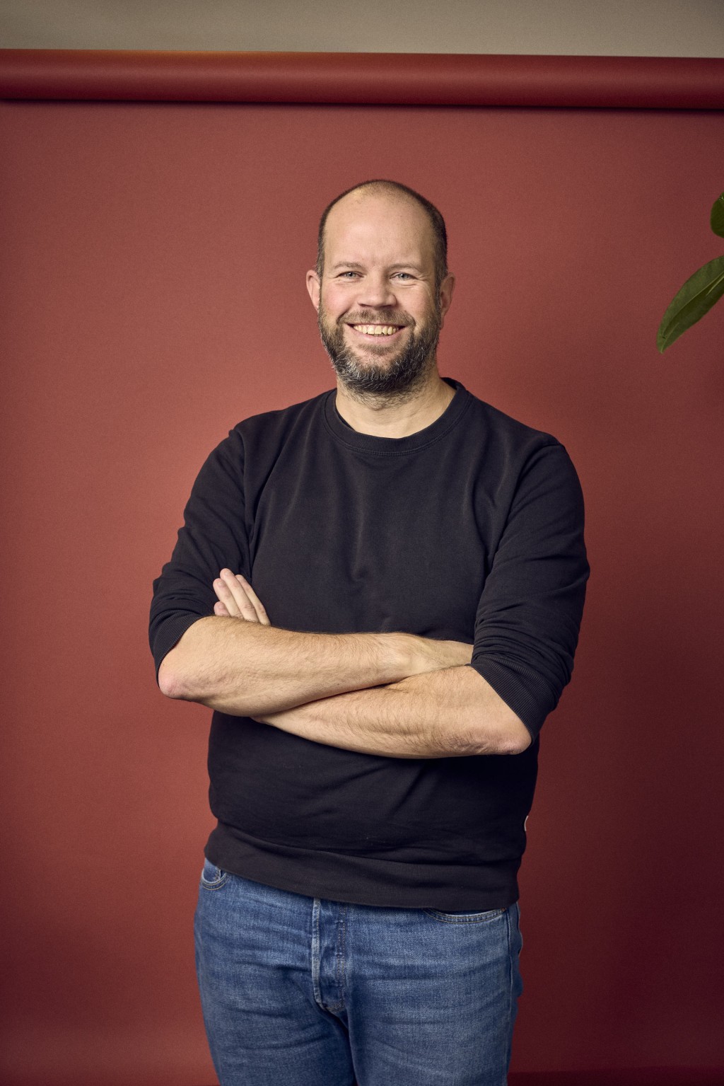 Sander Strijbos staat voor een rode backdrop met een donkerblauwe trui.