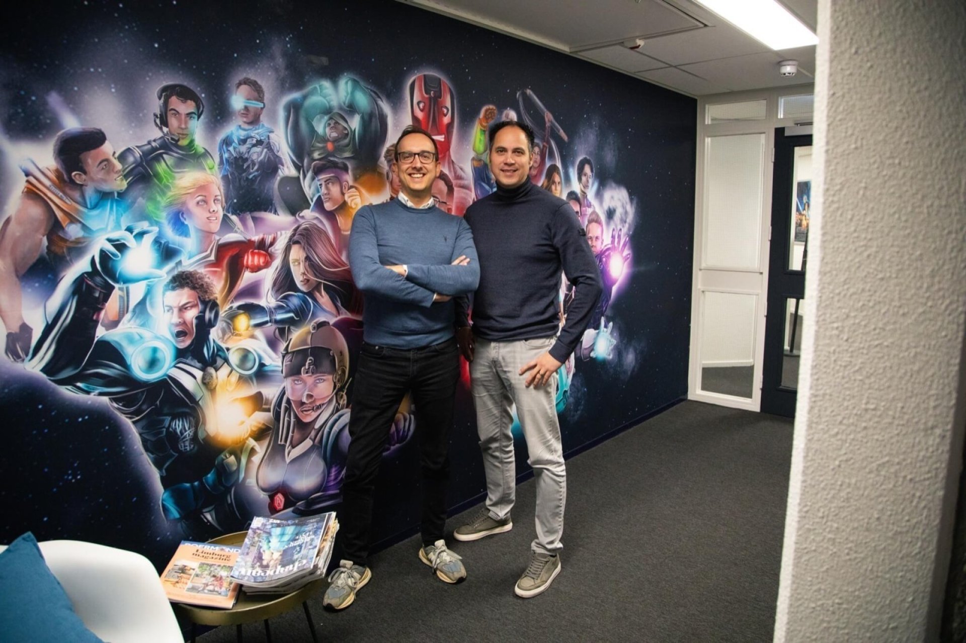 De directie van Appart Paul Cremers en Owen Manusama, voor een muur met superhelden in de hal van het kantoor.
