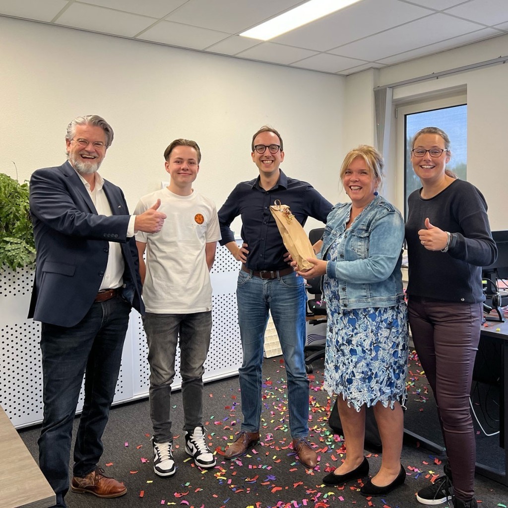 Vijf mensen vieren in een kantoorruimte een dubbele mijlpaal, met confetti op de vloer en een cadeauzakje: het negenjarig bestaan van het bedrijf en het behalen van een finaleplek voor de Roerstreekprijs.