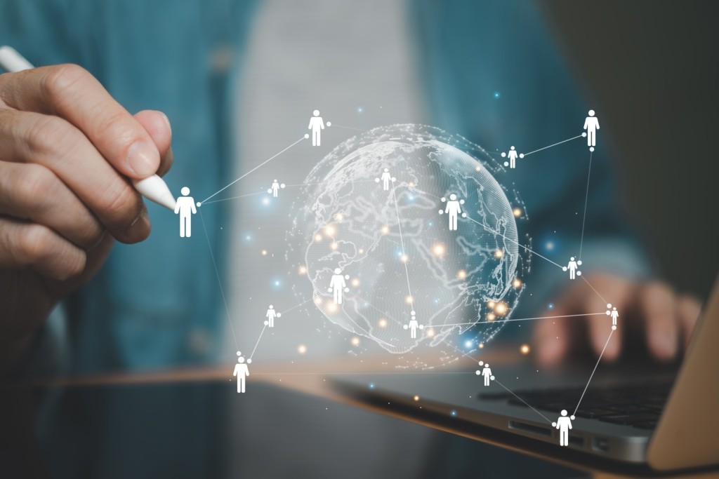 Hand die met een stylus een digitaal wereldnetwerk tekent waarin mensen wereldwijd met elkaar verbonden zijn.