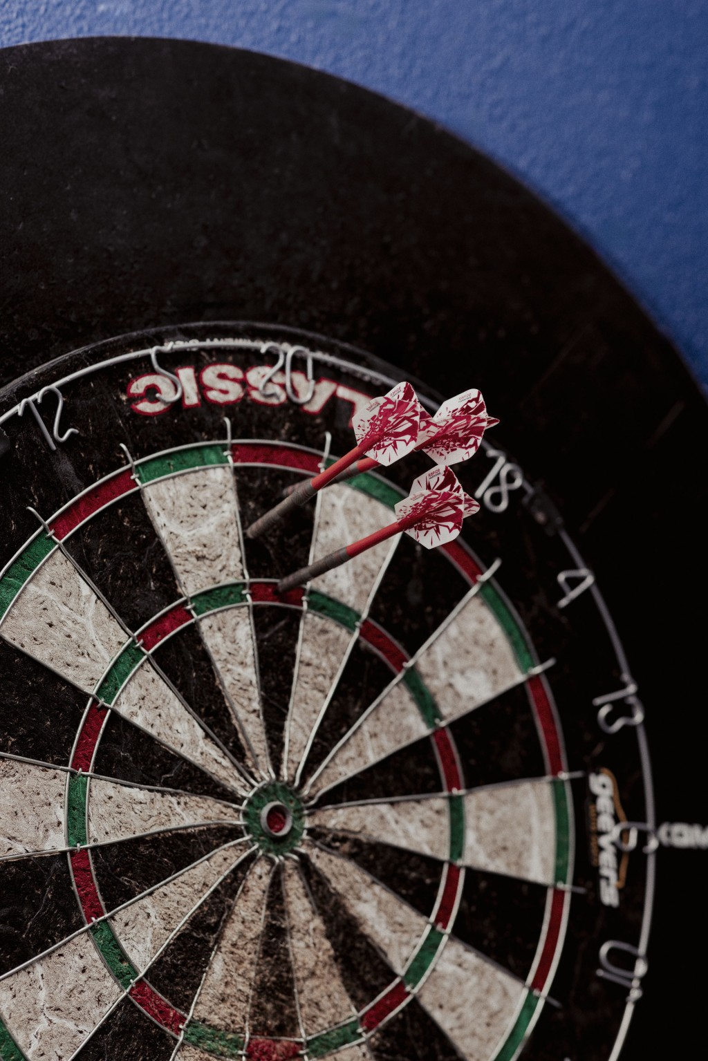 Een dartbord met drie rode darts aan een blauwe muur