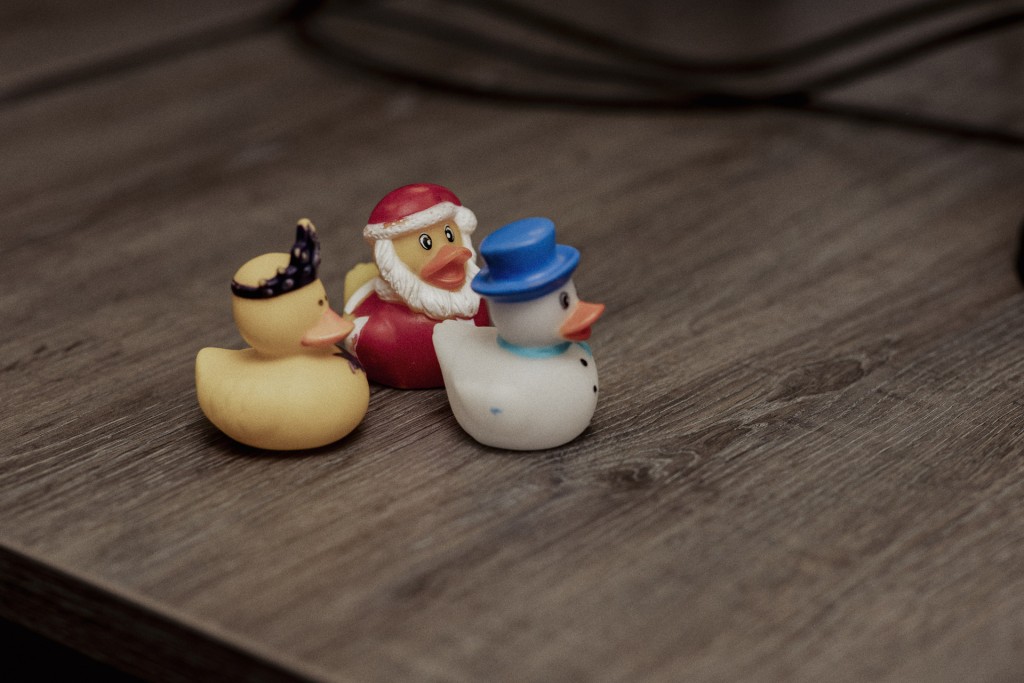 Drie kleine rubberen badeendjes in verschillende kleuren staan op een houten tafel